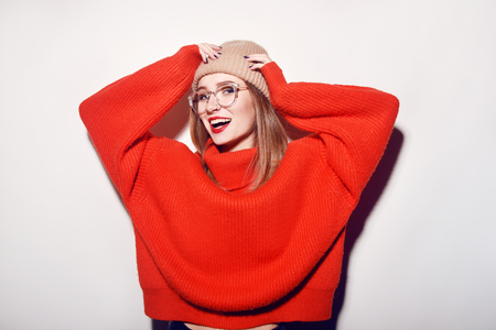 Happy Smiling Hipster Girl in knitted red sweater and hat having fun. Cute girl in glusses with piercing in the nose. Winter or Autumn Warming Up Concept.の写真素材