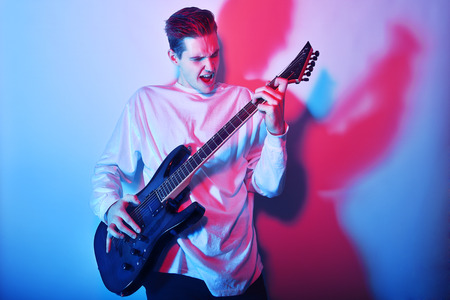 Portrait of a young man artist singing, screaming, playing an electric guitar Hobby, music concept....