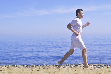 Man running on sunny beach. Unrecognizable body jogging on ocean beach. Man running on tropical beach. Attractive man enjoying nature. Man running on the beachの写真素材