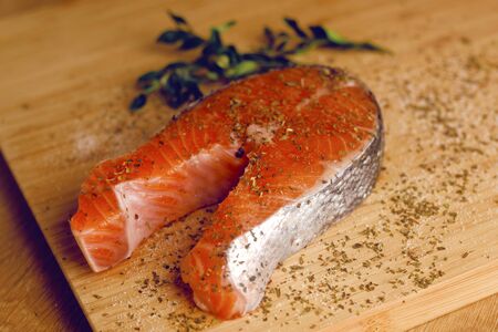 Photo of salmon. Fresh red fish, white veins, rich color. Fish seasoned in spices, dried basil, salt, pepper. Ringfish Fish. Salmon in a wooden plate for cutting basil marinade. Recipe Fish section.の写真素材
