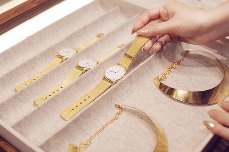 A girl buys a watch. A gold watch lies on the counter, a thief in a jewelry store. A beautiful hand takes a watch.の写真素材