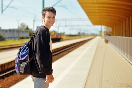 Man on train station, travel. Student in railway station. Smile freelance man. Boy with backpack waiting in a train station in sunny day smile.の写真素材