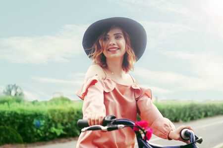 The girl in a beautiful pink dress and black hat rides a bicycle.の写真素材