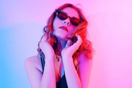Beautiful girl in neon. Fashion photo of a short-haired girl, dancing, sun glasses. Girl in red and blue light posing.の写真素材