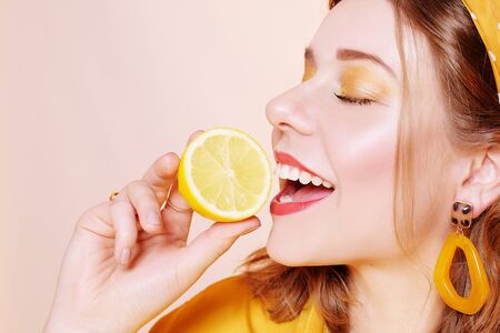 A beautiful portrait of a girl who eats a lemon, bites off a slice of lemon, a girl sniffs a lemon. Health, skin beauty, lemon-based face masks, lemon diet. Girl with bright yellow make-up.の写真素材