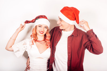 Couple on a white background in santa hats. The girl and the guy are smiling, new year, christmas. Woman in a beautiful white dress and pink hair, in accessoriesの写真素材