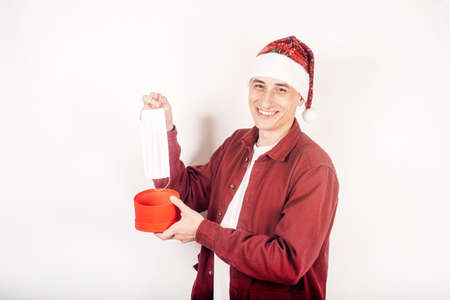 A man in a santa hat. The man holds the gift in his hands and takes out a mask from there. Covid.の写真素材