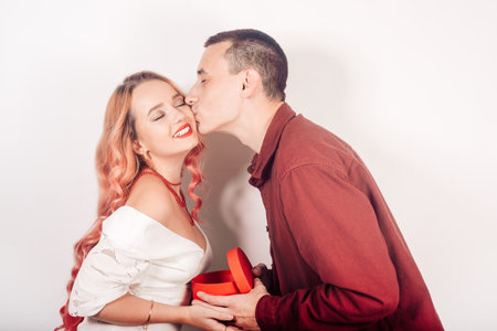 A pair of lovers on a white background. A man gives a woman a gift for the new year, christmas. The guy holds the box in his hands, the girl smilesの写真素材