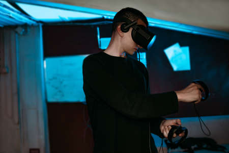 A man at home wearing virtual reality glasses. Holds controllers in his hands. Guy plays vr games