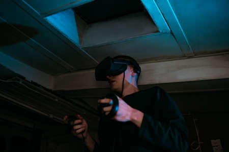 A man at home wearing virtual reality glasses. Holds controllers in his hands. Guy plays vr gamesの写真素材