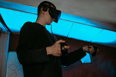 A man at home wearing virtual reality glasses. Holds controllers in his hands. Guy plays vr games