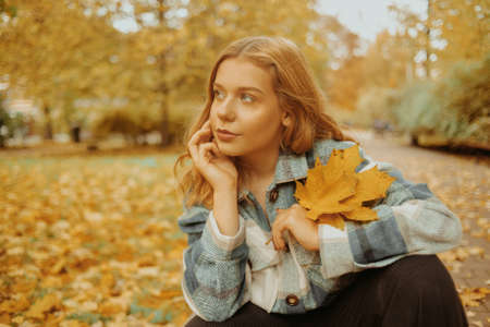 A woman is sitting in an autumn park. Girl teenager on a background of autumn leaves. Fashion photo