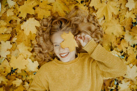 Beautiful girl lies in the park in autumn. A teenager in a yellow sweater on a background of orange...