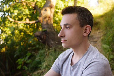 A man sits in a forest in nature and looks into the distance. Guy on vacation portraitの写真素材