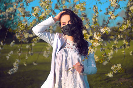 A beautiful girl in a mask stands in blossoms. You can go outside during quarantine, but only in...