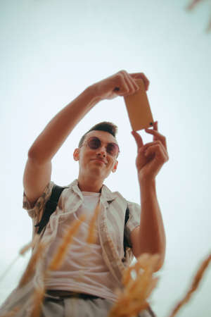Photo of a man from below taking a photo of the field on his smartphoneの写真素材