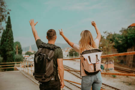 A couple with backpacks travels the world. The guy and the girl delight and raise their hands aloud. Lovers wait for their train and enjoy the viewの写真素材