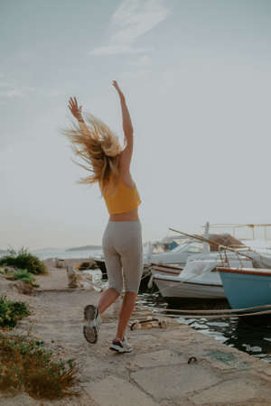 Joyful girl jumps on the background of the sea. Vacation, freedom. Woman on the background of yachts and shipsの写真素材