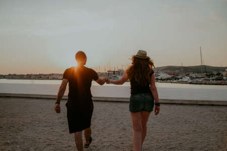 A couple walks near the sea against the background of sunset. Lovers run on the beach Honeymoon....