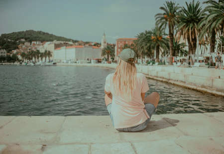 The girl sits on the seashore and looks into the distance. Model on the background of palm trees and plate city Croatiaの写真素材