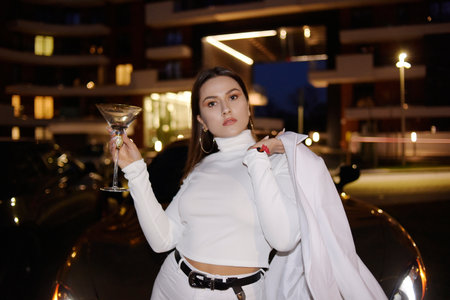 Chic girl drinks a drink in a glass on the street near the car, a golden car, Dubai. Fun, girl lives...