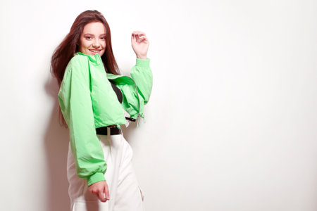 A girl dances in a green jacket a beating light, a fashionable teenager moves, laughs, dances, a party. Brunette with long hair.の写真素材