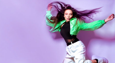 Girl brunette with long hair on a purple background jumps, flies. Dancing, hip hop.の写真素材