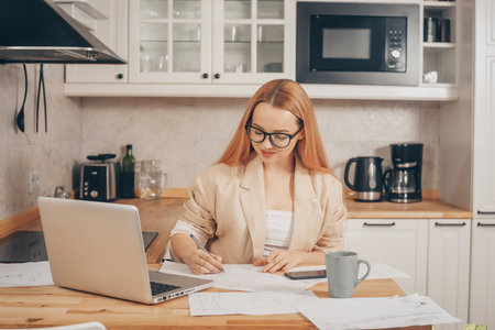 Woman at laptop works from home, student, teacher. A beautiful blonde in a jacket and glasses looks into a laptop and writes something down. Online training, work freelance accountant.の写真素材