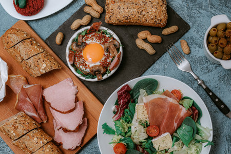 Lots of food and dishes in the background. Meat platter and Camembert cheese with baguette. Salad with prosciutto. Olives. Perfect fried eggs with mushrooms and spices. Vegan vegetable cutlets and peanuts. Fork. Food delivery.の写真素材
