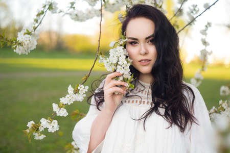 Incredibly tender girl in blossoms, on a background of a tree with white flowers, a model. Brunette...