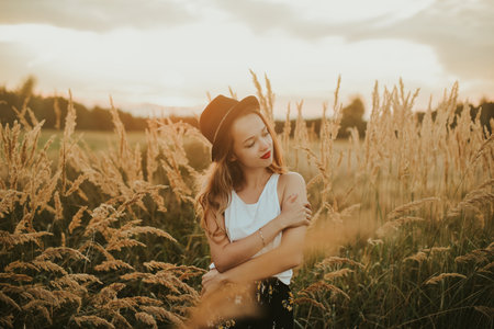 Beauty Girl Outdoors enjoying nature. Pretty Teenage Model in hat running on the Spring Field, Sun Light. Romantic young blonde girl in a wheat field. Blowing Long Hair. Happy girl smile, sunset.の写真素材