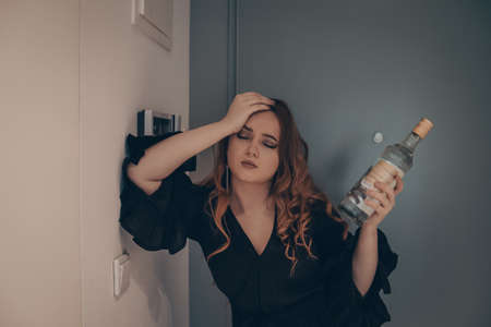 The drunk girl came home after the party. Beautiful woman on the doorstep tired with a bottle of...