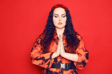 Beautiful girl on a red background. Brunette with red roots of curled hair in a red dress and red lips. Thanks in Japanese.の写真素材
