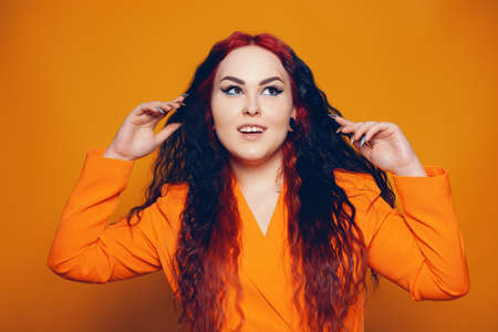 A woman with red roots and black hair. Unusual hairstyle, hairdresser, wind in your hair. Girl on a yellow background in an orange dress. Fashion and beauty.の写真素材
