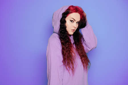 Woman in a blue sweater on a purple background posing. Beautiful brunette with long hair. Eyeliner and trendy makeupの写真素材