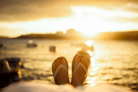 Legs of a girl against the background of the ocean and the sea, beautiful sunset and travel, romance, weekend, tourists. Solo travelの写真素材