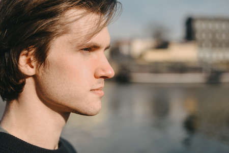 Profile of a man on a sunny day. The guy on the background of the river in Europe looks into the distance. Portrait of a guyの写真素材