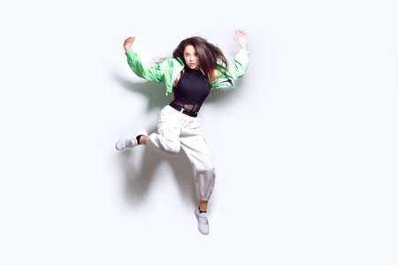 A girl dances in a green jacket a beating light, a fashionable teenager moves, laughs, dances, a party. Brunette with long hair. Girl in flight, jumping.の写真素材