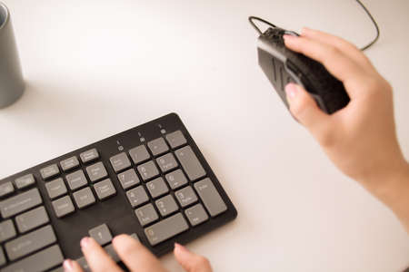 The English keyboard is on a white table and a mouse. Female hands are typing something.の写真素材