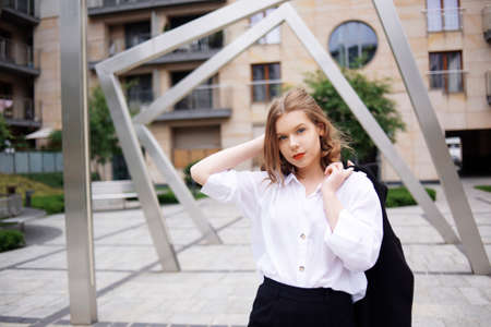Student, manager, realtor, girl in a white shirt on the background of the building posing. Beautiful blonde with short hair. Model with red lips and a black jacket.の写真素材