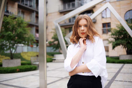 Student, manager, realtor, girl in a white shirt on the background of the building posing. Beautiful blonde with short hair. Model with red lips and a black jacket.の写真素材