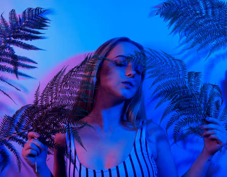 High Fashion model girl in colorful studio. Portrait of a girl in neon in tropical leaves. Chic Gorgeous blonde posing in the club on vacation.の写真素材