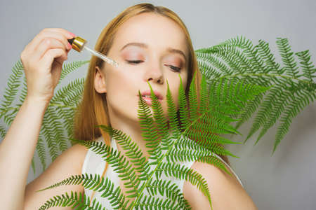 Girl on the background of tropical leaves natural cosmetics and medicines. The model holds a bottle and oil for the face and applies it to the skin. Bottle with a pipette.の写真素材