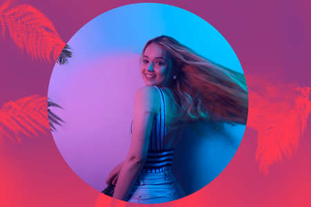 A model in neon poses. Fashion photo of a girl in a swimsuit and shorts in pink-blue light. Girl on a background of tropical leaves summer photo. Beautiful blondeの写真素材