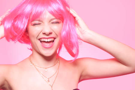 The girl in a pink wig, on a pink background, is happy, grimaces, smiles. Bright photo of a teenager, smart, party, dance. Anime pink cute girlの写真素材