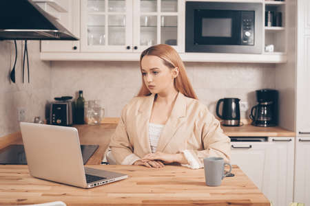 Woman behind laptop works from home. The student submits a report online. The girl teaches courses, lectures on the Internet. Freelance earnings. The model is gesturingの写真素材