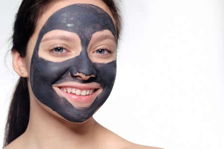 Teenager girl in a black mask, natural photo of a real mask on a young girl. Texture dark cream. Model on a white background smokes skinの写真素材