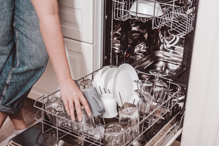 Built-in dishwasher, dishwashing. A woman loads washed dishes, cups, glasses. A woman's gentle hand puts something in the dishwasher or pulls out, unloads.の写真素材