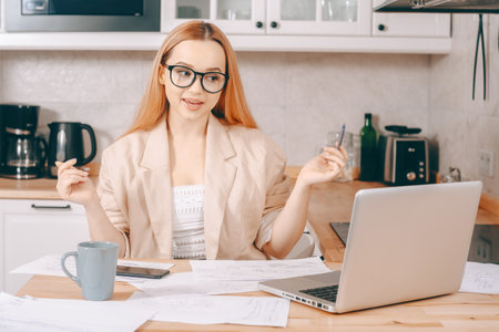 Woman behind laptop works from home. The student submits a report online. The girl teaches courses, lectures on the Internet. Freelance earnings. The model is gesturingの写真素材