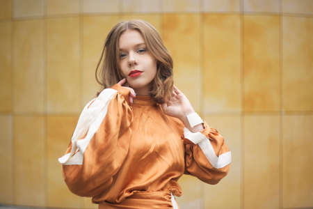 Portrait of a girl with short hair and red lips. Beautiful model with blue eyes in a fashionable brown dress. Model posing against the wall. Gorgeous short hair.の写真素材
